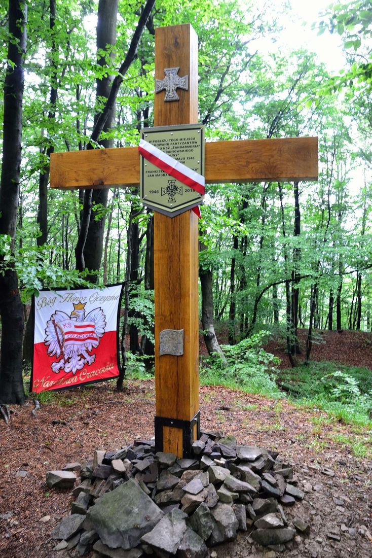Drewniany krzyż z tablicą upamiętniającą partyzantów, stojący na kamiennym kopcu w buczynie w partiach szczytowych Grodziska.