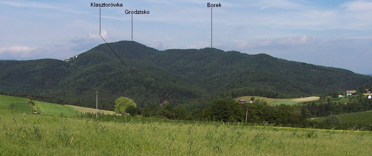Szeroki letni widok na grzbiet Grodziska z Góry Św. Jana, z wrysowanymi w zdjęcie podpisami wierzchołków: Klasztorówka, Grodzisko, Borek (15.06.2007). Proporcje 2,37:1, ale tylko i podpisy wypalone w obrazie.