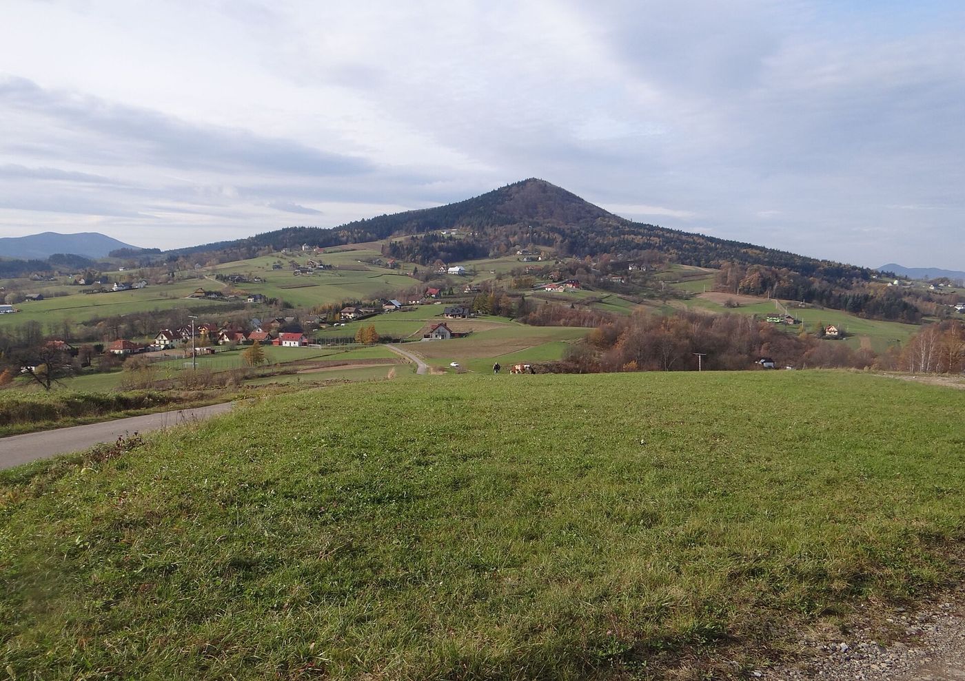 Kostrza od wschodu, z Rupniowa: prawie symetryczny stożek góry wyspowej, listopadowa łąka i rozproszona zabudowa na pierwszym planie