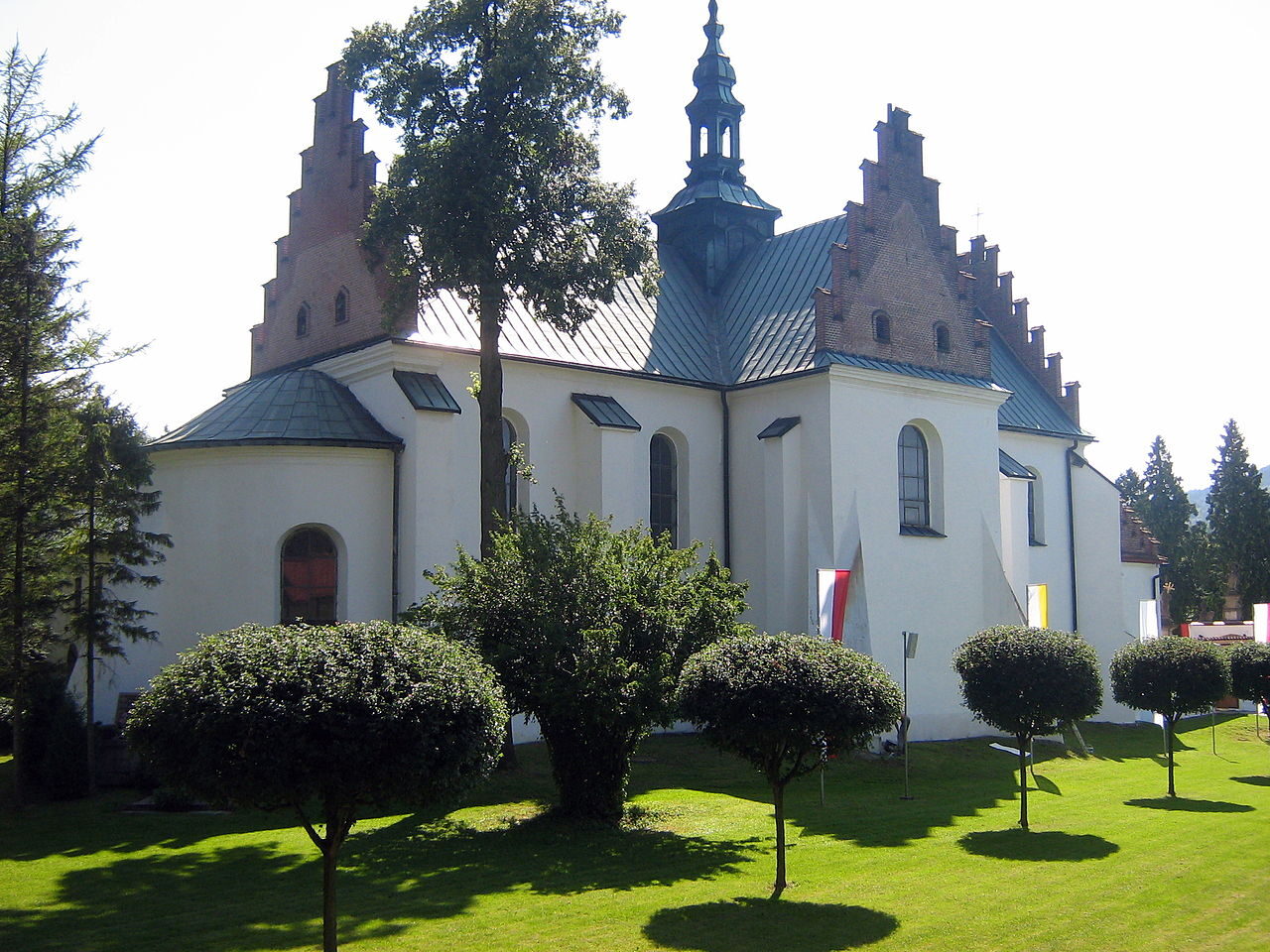 Kościół opactwa cystersów w Szczyrzycu — białe mury, schodkowe szczyty i sygnaturka, przed nim strzyżone krzewy na trawniku