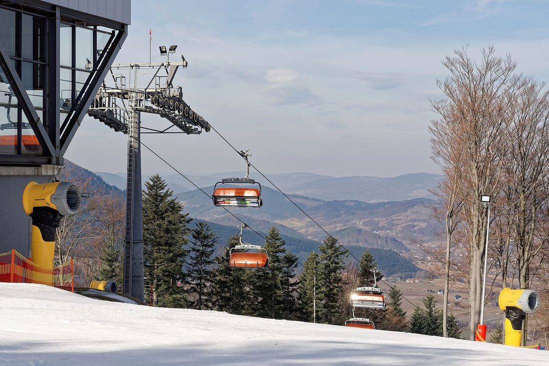Górna stacja kolei krzesełkowej Kasina Ski na Śnieżnicy zimą: pomarańczowe krzesełka nad zaśnieżonym stokiem, armatki śnieżne i panorama doliny.