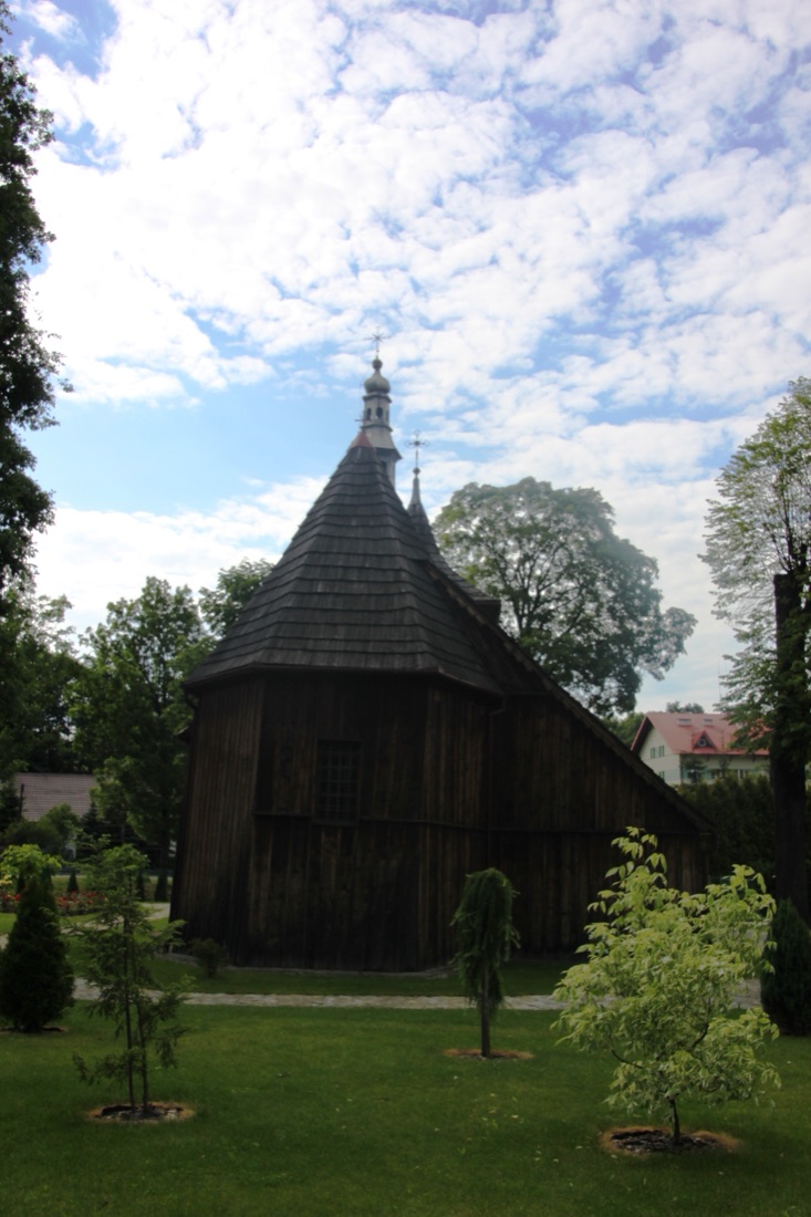 Kościół od strony prezbiterium: ciemne, gontowe ściany, trójbocznie zamknięta absyda i wieżyczka na sygnaturkę nad dachem.